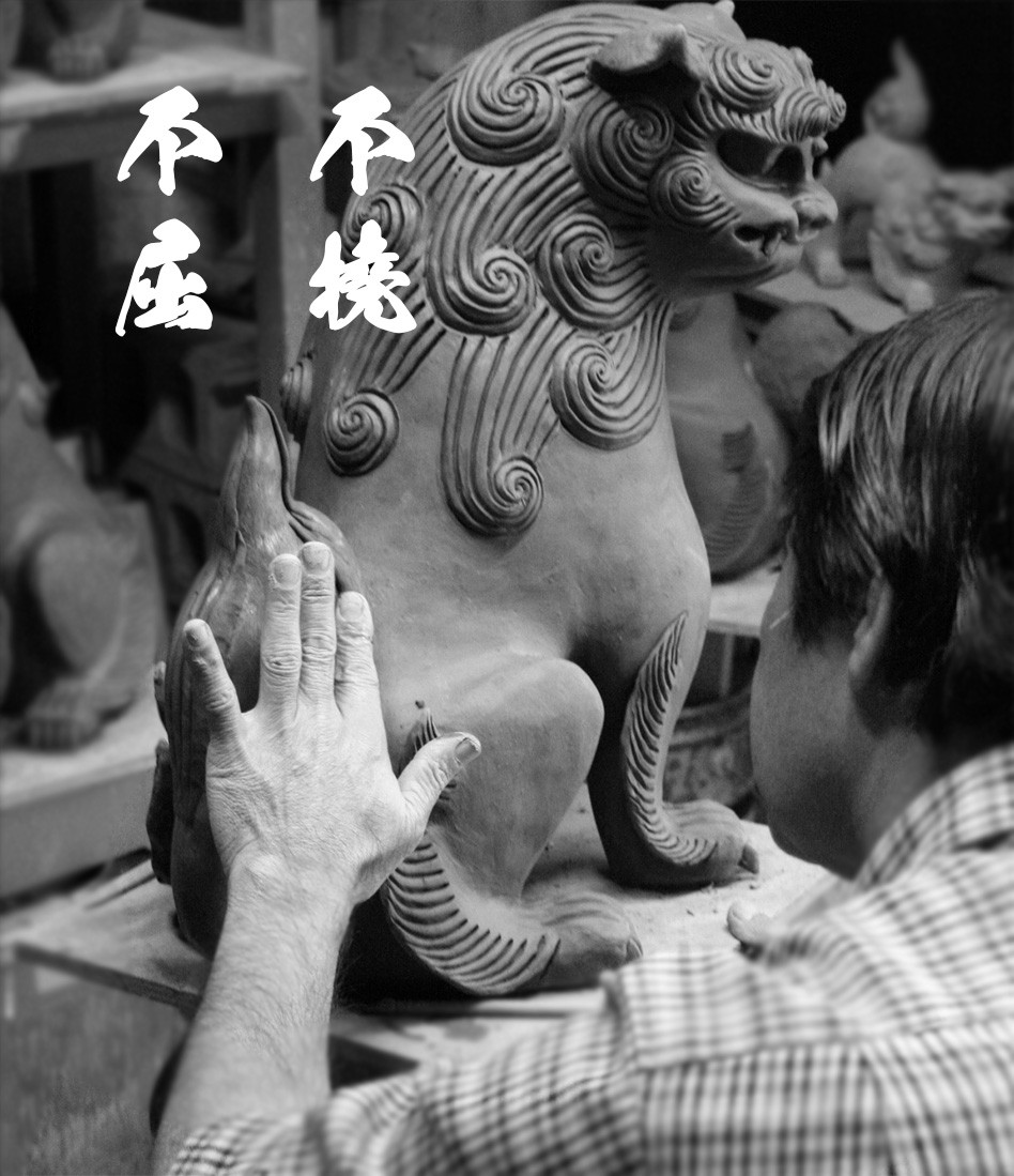 50代の新垣信一がシーサーに手を添え、造形を確かめる白黒写真