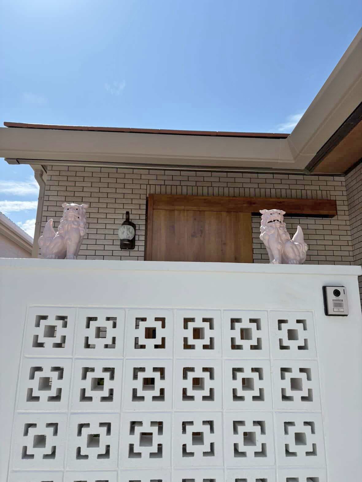 青空の下、白い門柱の左右に設置されたピンクのシーサーの一対