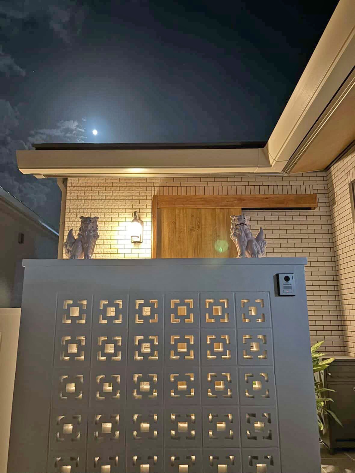 夜、玄関の灯りに照らされる白い門柱とピンクのシーサーの一対