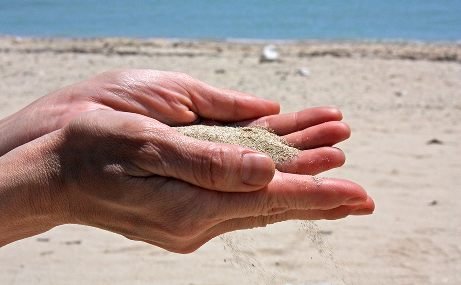 嘉陽の砂浜の写真、砂を手に取って細かな砂が手からこぼれていく写真、背景は海